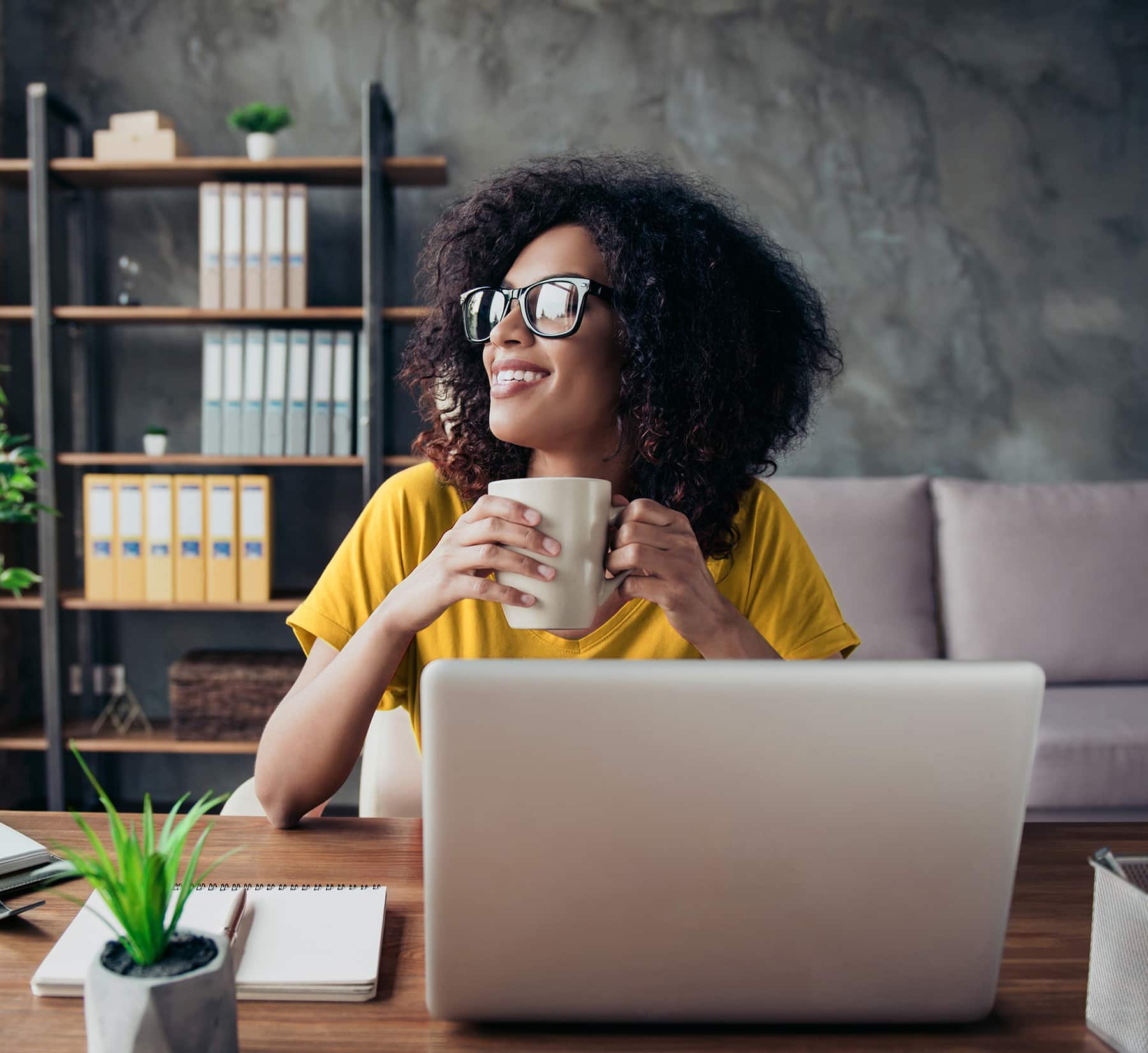 Woman holding coffee mug at desk with laptop.